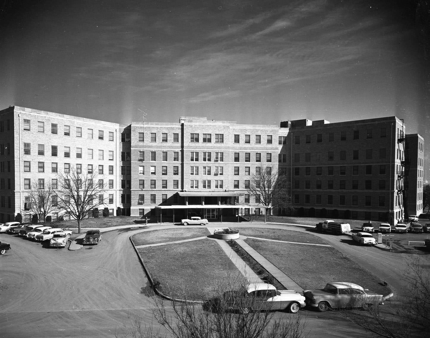 The exterior view of the Hendrick Hospital in Abilene, Texas, 1950s. The building is about six stories high and there are cars parked on the street in front of the hospital.