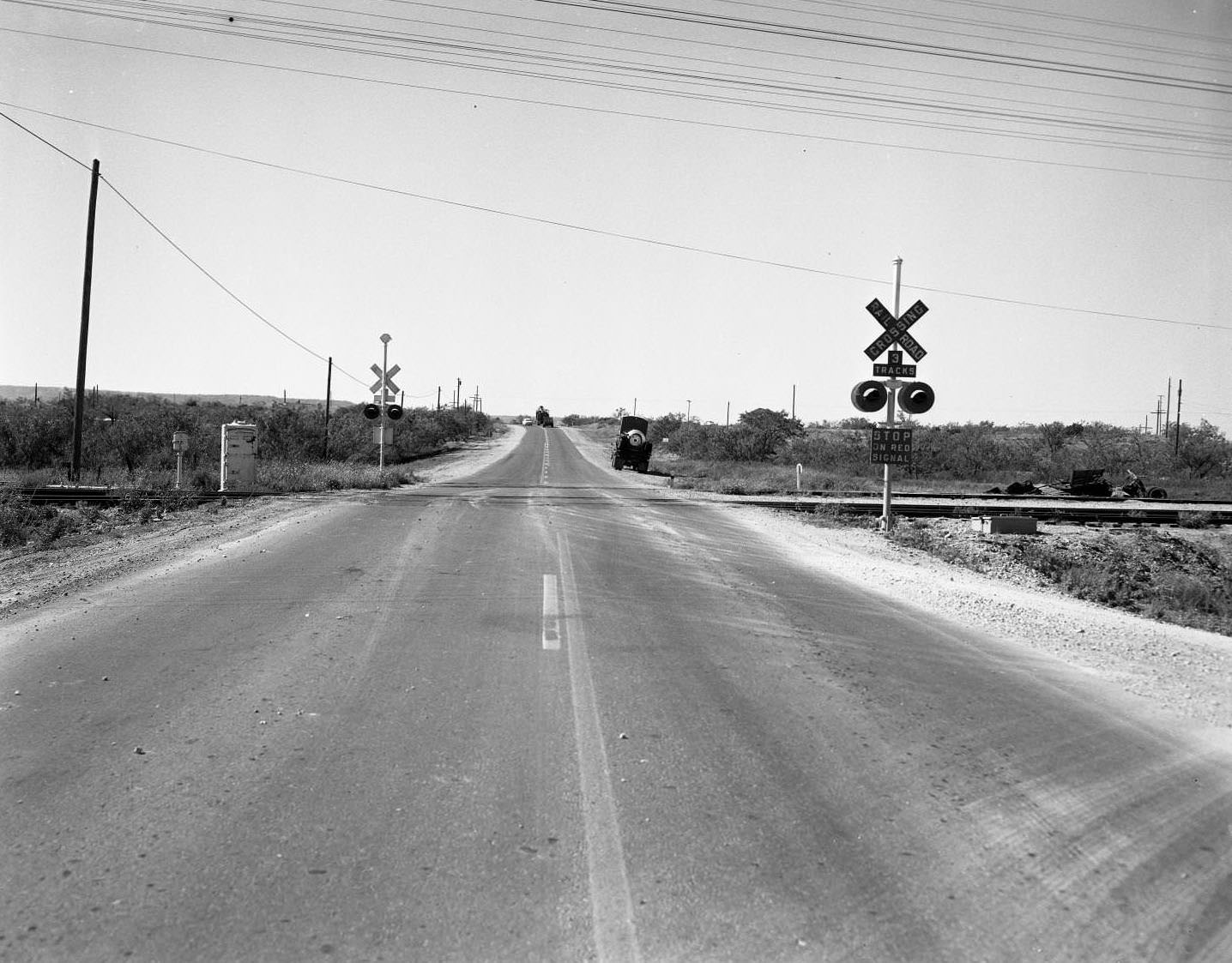 A highway accident scene and a railroad crossing. There is a truck parked on the right side of the road, 1955