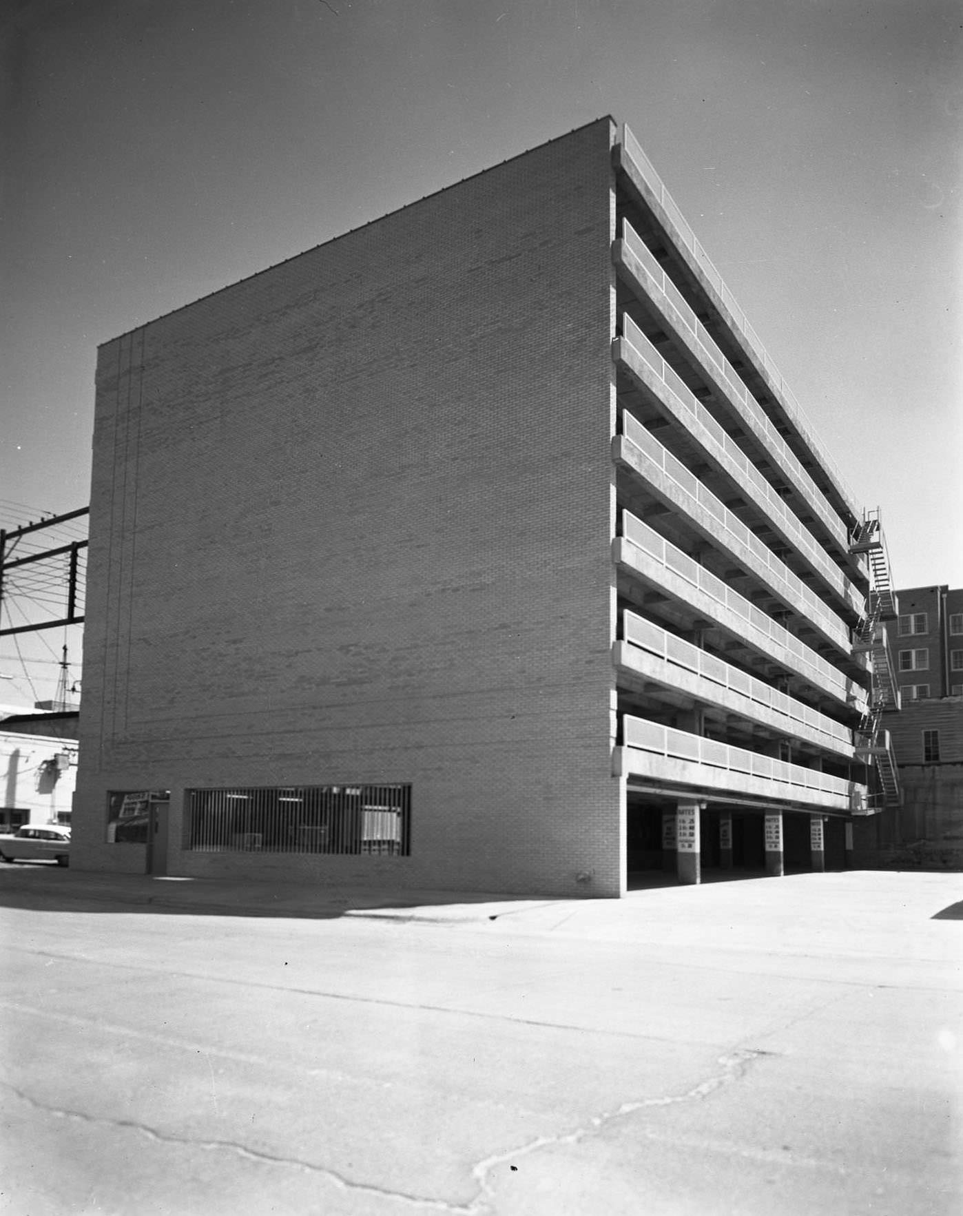 Parking garage at F and M Bank, 1955. The building has seven above ground levels. There are buildings, a car, and power lines behind it.