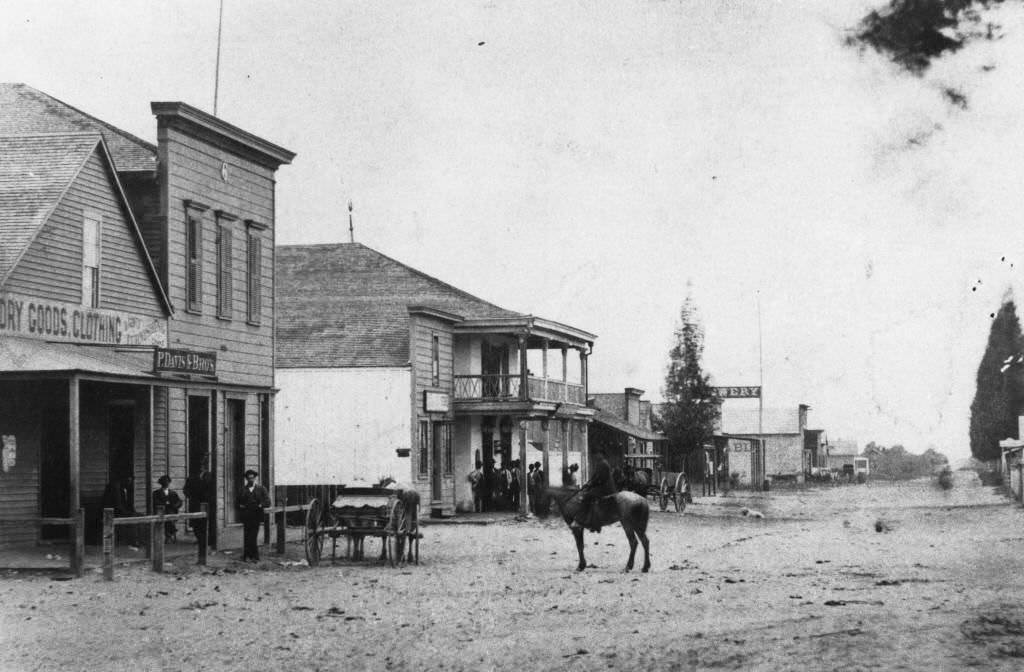 View of Center Street (now Lincoln Ave.) looking west past Los Angeles Street (now Anaheim Blvd.); view shows dirt road and buildings on the north side of the street, 1873