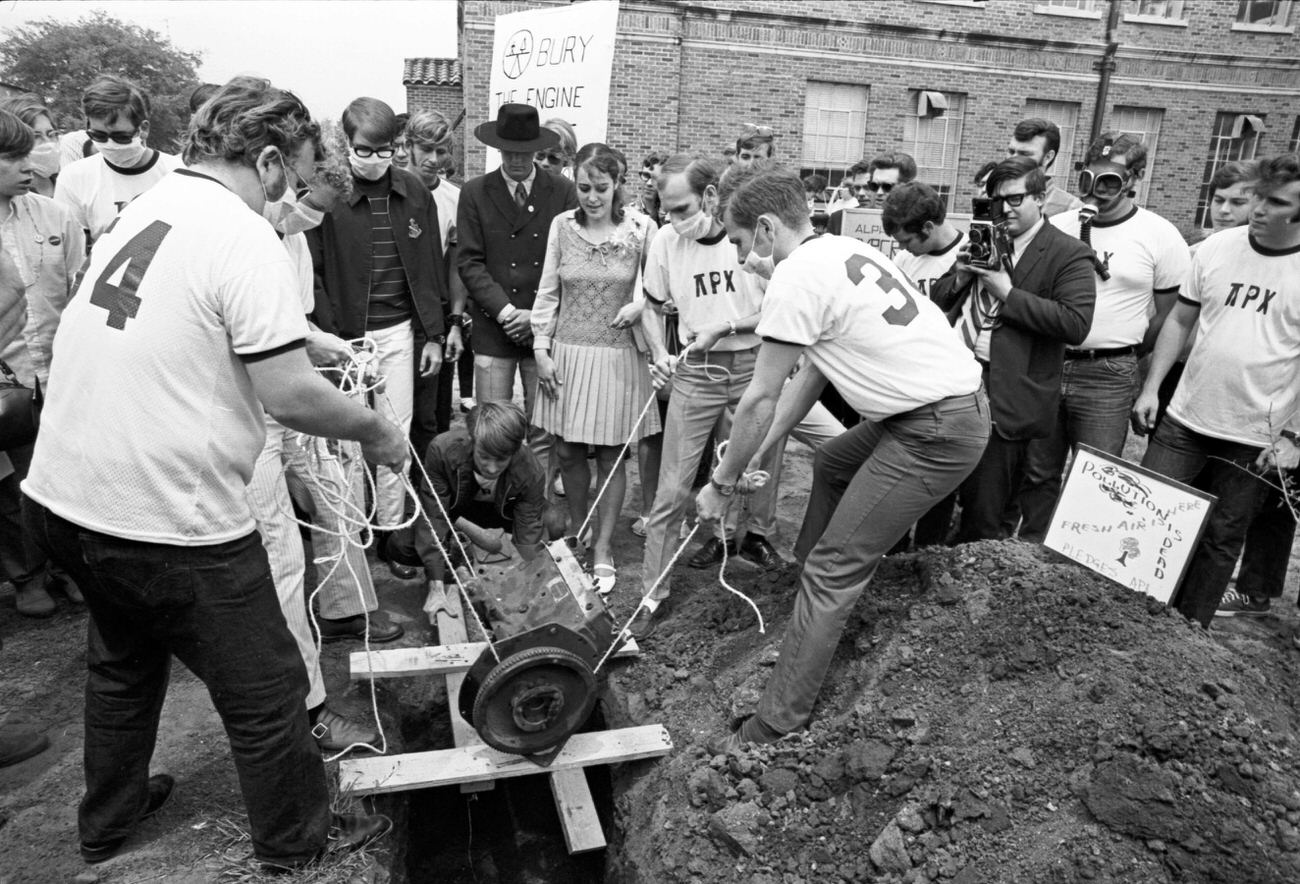 Students at The University of Texas at Arlington gathered around before dropping an internal combustion engine into a shallow grave on campus for Earth Day, 1970