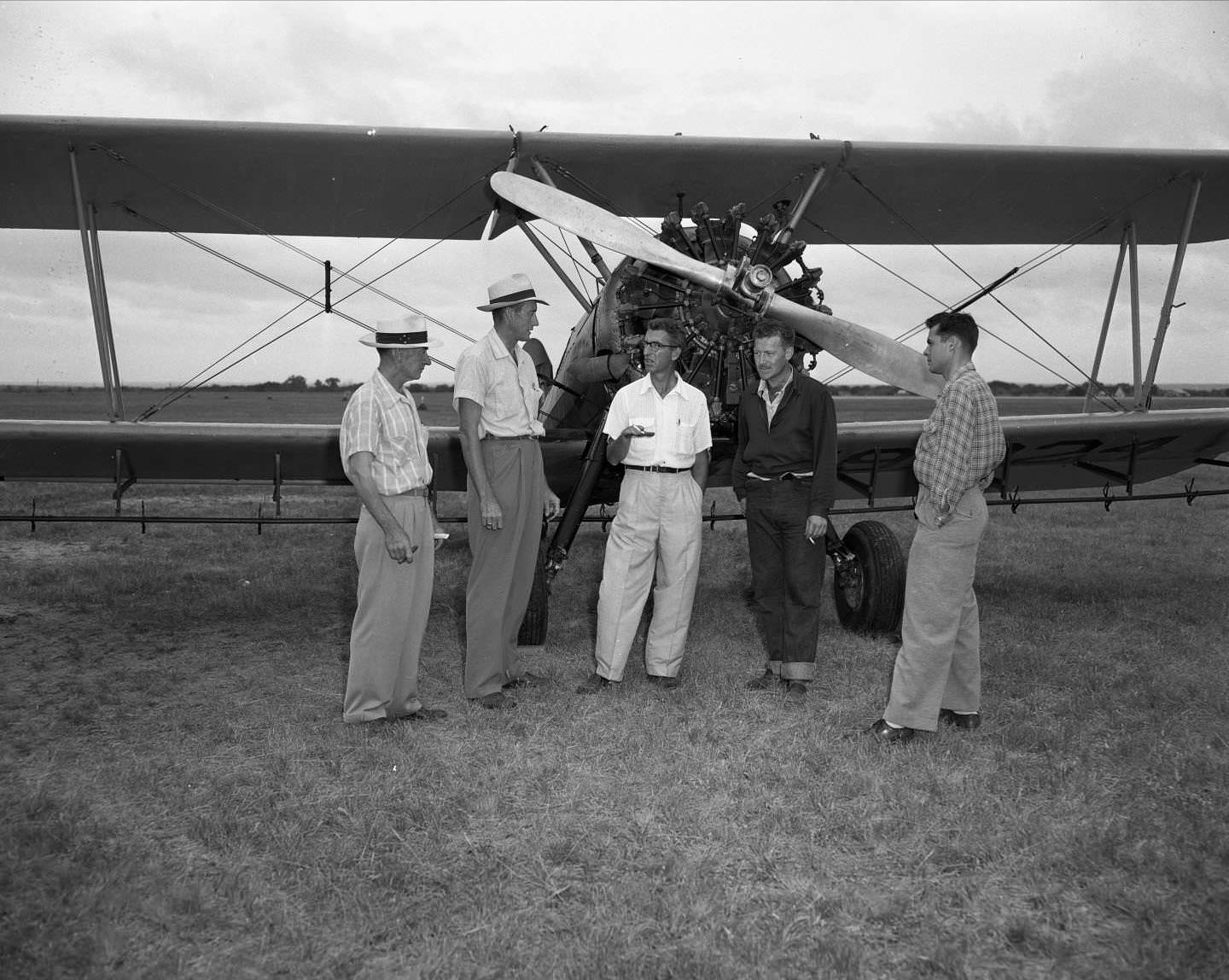 Five men standing in front of prop plane, 1954