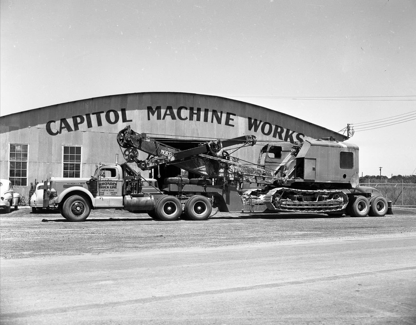Flatbed truck loaded with crane parked in front of Capitol Machine Works building, on 4824 East 1st Street in Austin, 1951