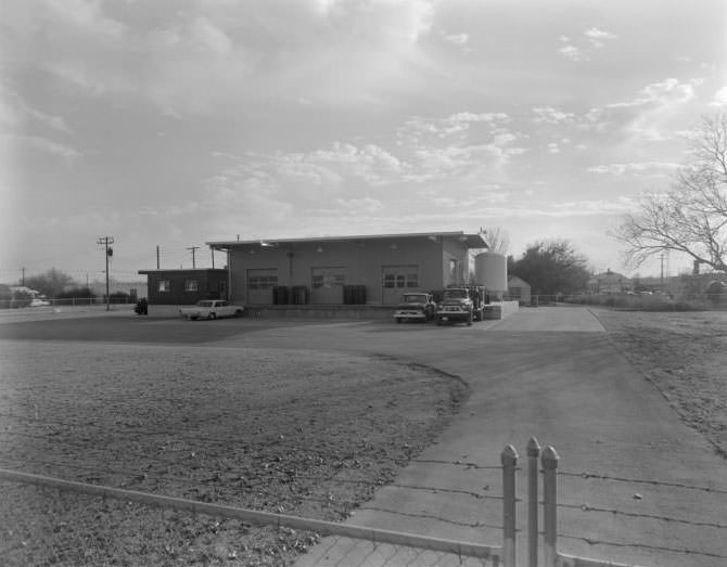 Exterior view of building with loading dock. 2 trucks and 1 car parked in front of dock, 1962