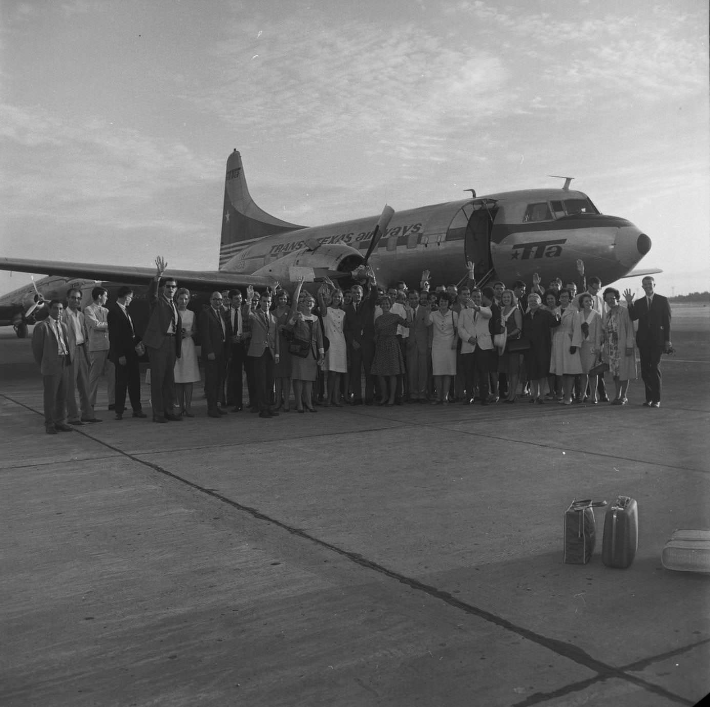 Passengers and crew wave goodbye on the tarmac before departure at Mueller Airport. Plane is Convair 240. TTA DC-3 in left background, 1966