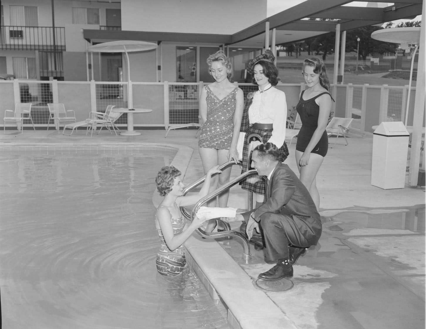 A man wearing a suit standing with four women at the pool at Imperial 400 Motel, 1962