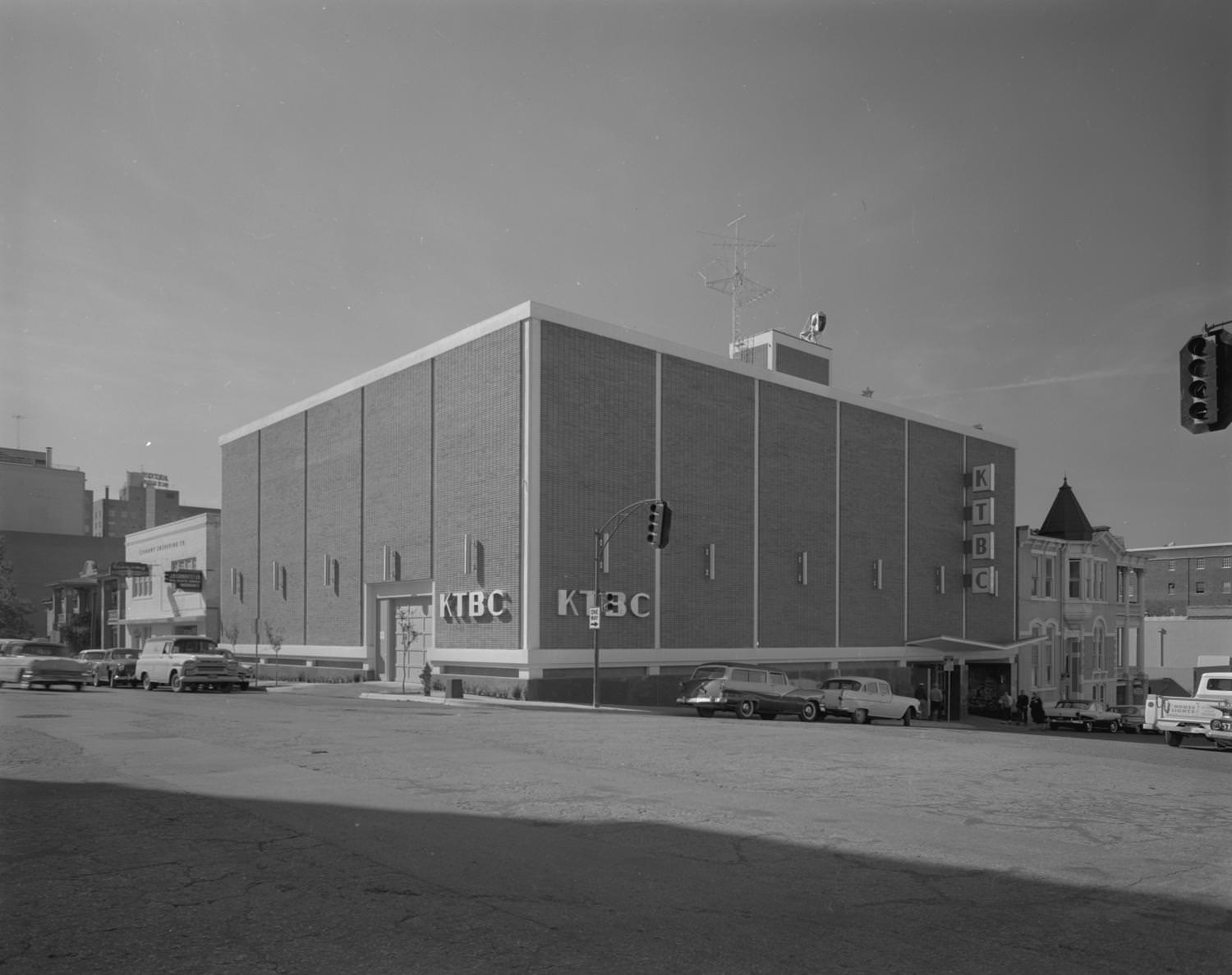 KTBC Studio on a street corner with traffic lights for an intersection seen in the foreground, and cars seen both driving and parked on each street, Austin, 1960