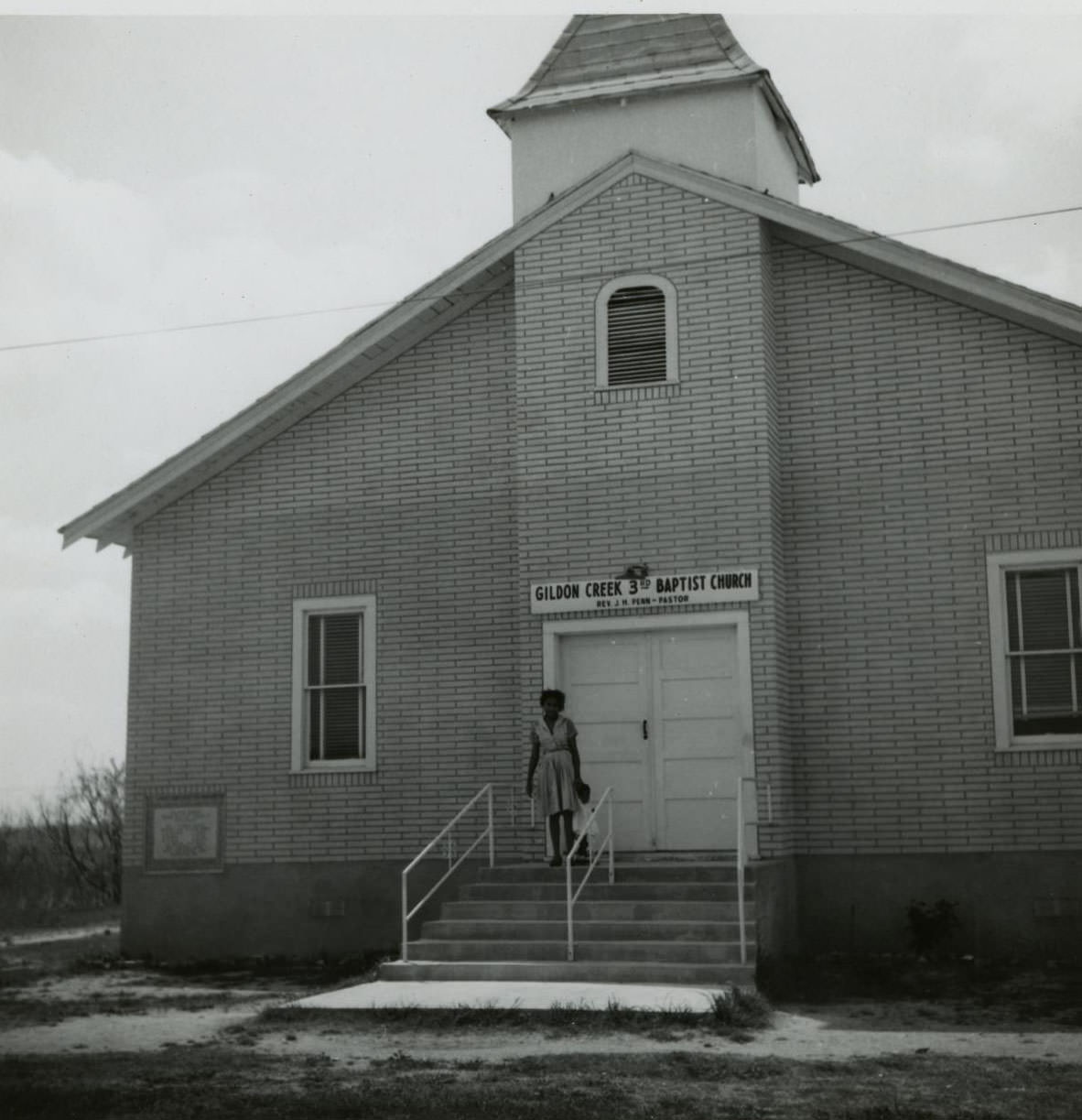 A woman standing on the front steps of the Gildon Creek Third Baptist Church building, 1962