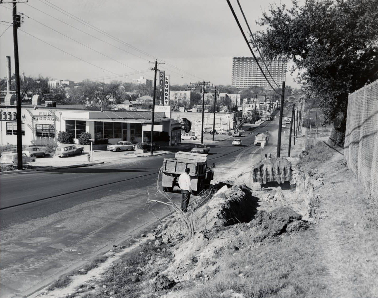 The 19th Street (now Martin Luther King Jr Blvd.) looking west from about Trinity, 1960 .Buildings line the left side of the street and construction vehicles and workers are on the right side.