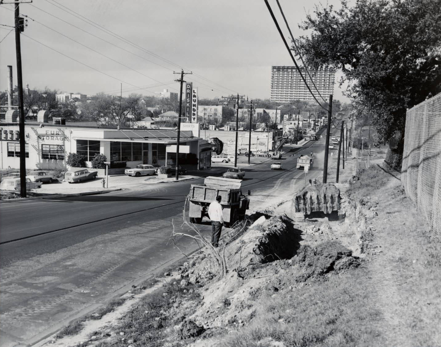 The 19th Street (now Martin Luther King Jr Blvd.) looking west from about Trinity, 1960 .Buildings line the left side of the street and construction vehicles and workers are on the right side.