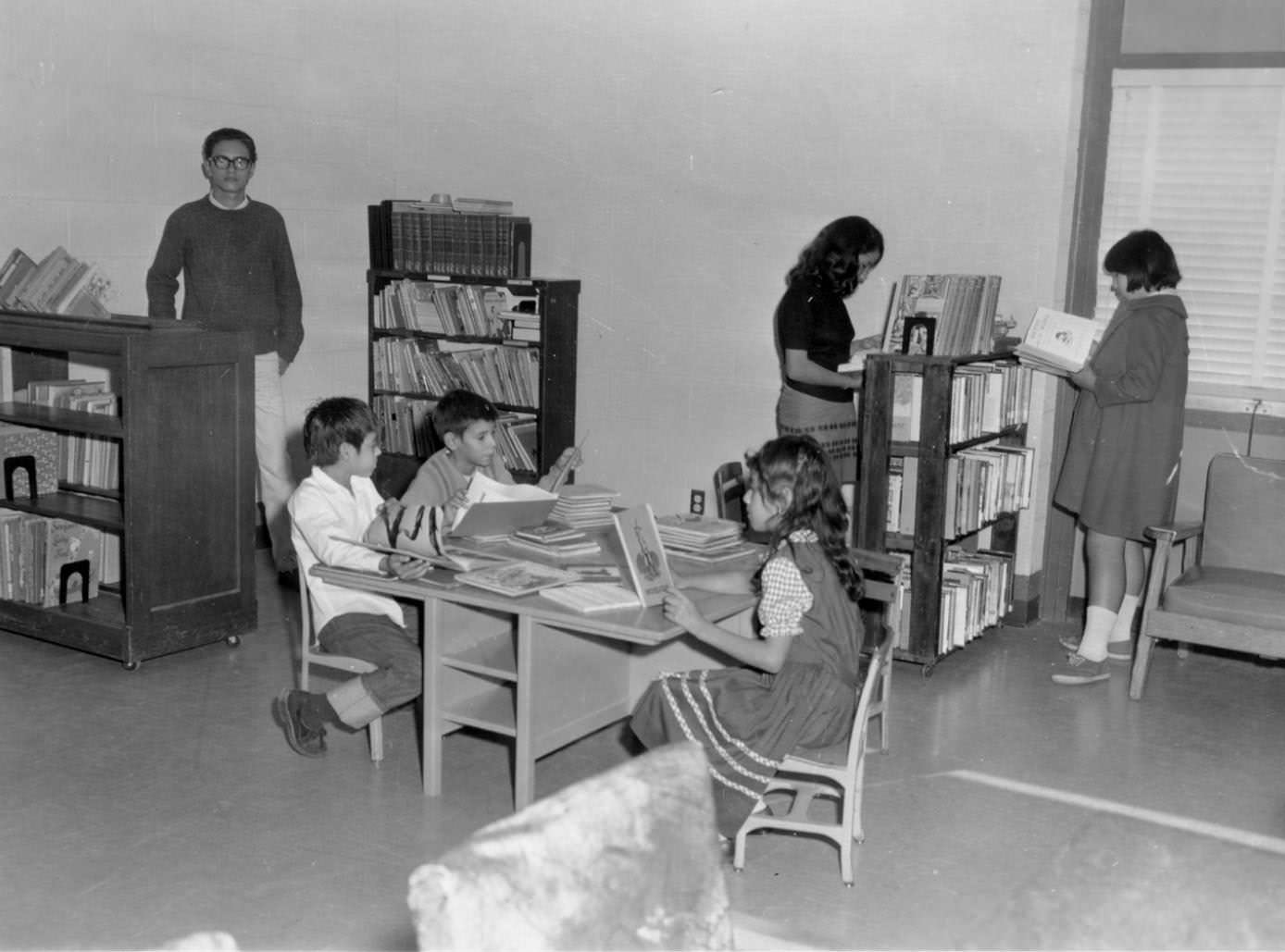 Children reading at the Pan Am Rec Center library, 1966. Three children sit at a child's table with books covering the tabletop in front of them.