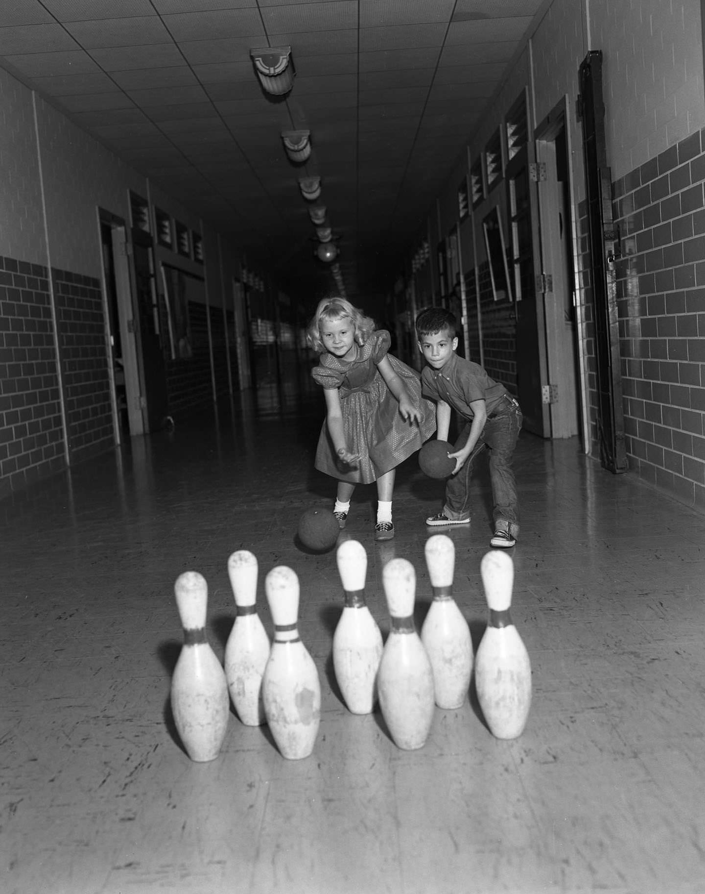 Two children bowling in a school hallway, 1961