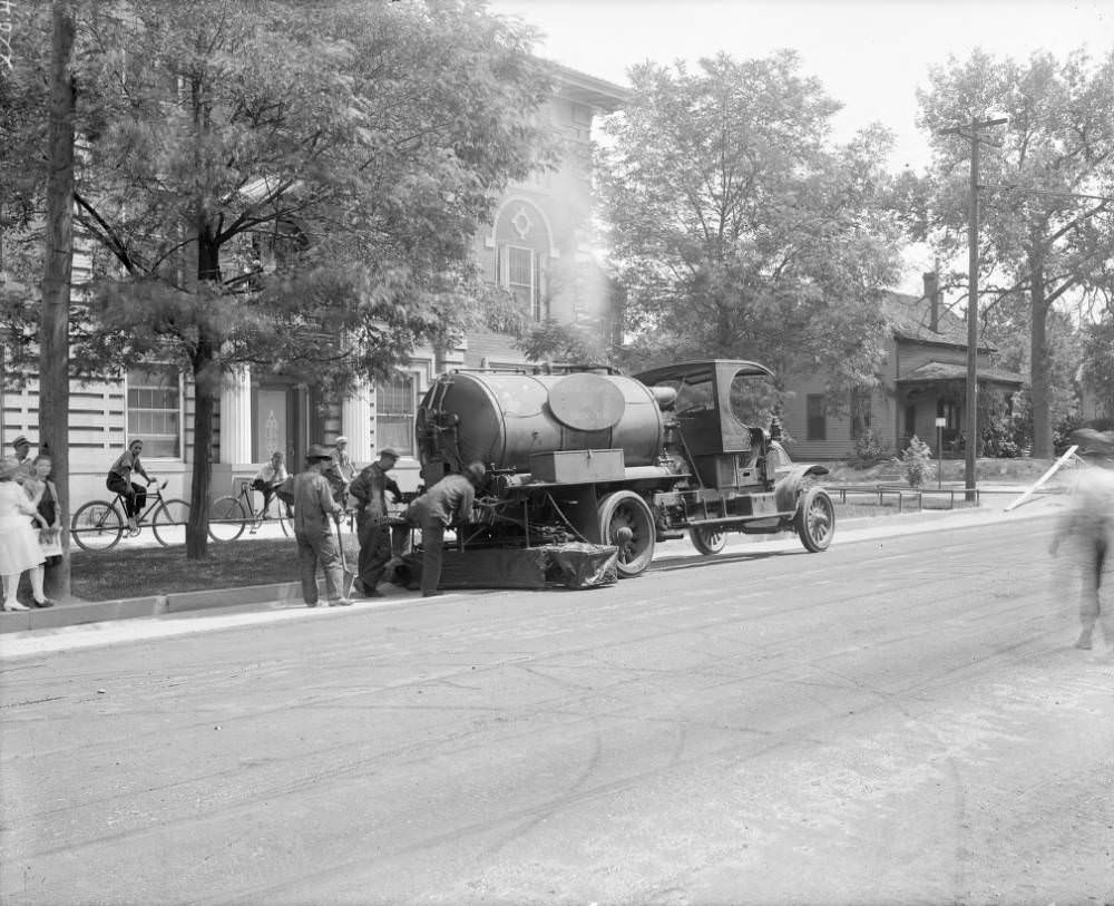 A truck applying oil to a street in Denver, Colorado; brick apartments and a frame house are in the background, 1905