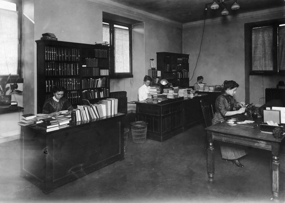 Women who include Frances Sims, Agnes S. Hall, Anamtille [?] McClung, and Louise Wells work at desks in the catalog department of the Denver Public Library at Colfax Avenue and Bannock Street in the Civic Center neighborhood of Denver, 1910