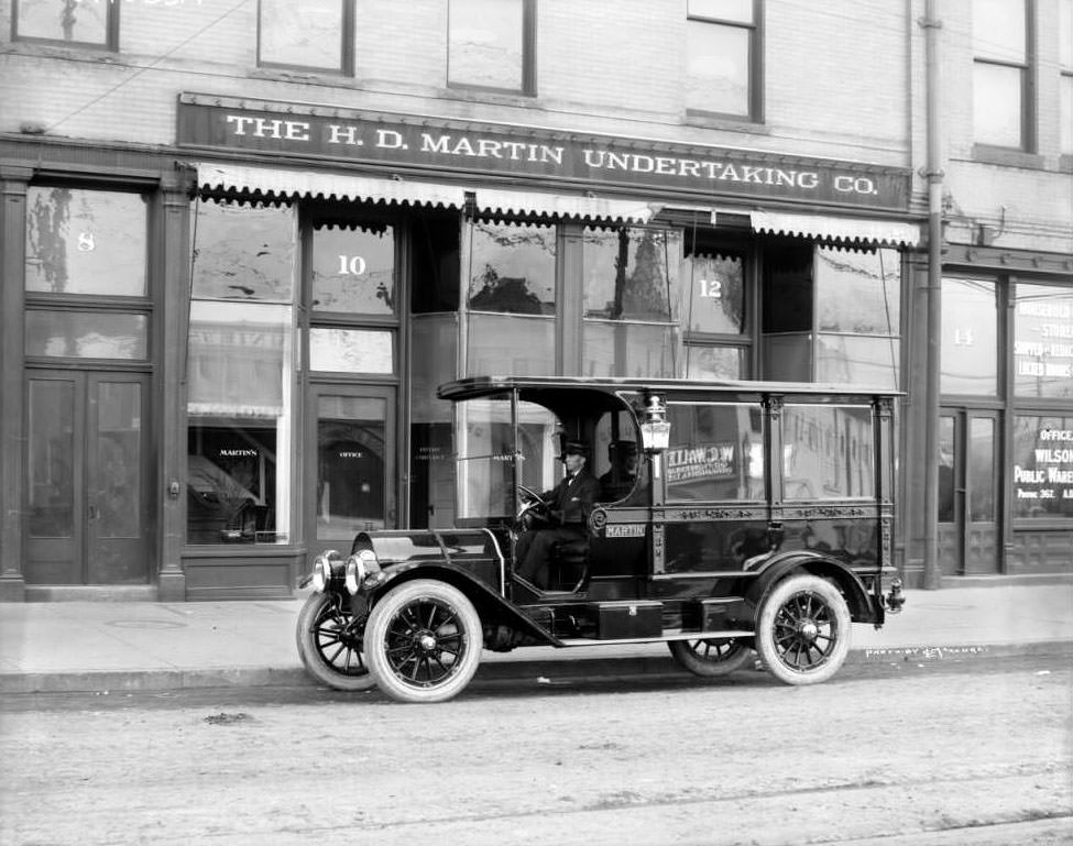 A driver sits in a hearse parked in front of the H. D. Martin Undertaking Co. at 10-12 West Colfax Avenue, Denver, 1900