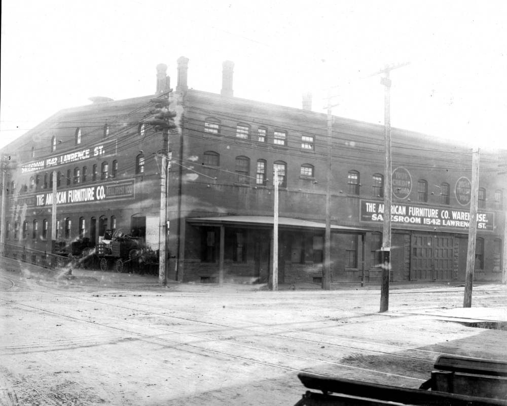 View of horse-drawn wagons, one filled with furniture, next to the American Furniture Company warehouse at 1542 Lawrence Street in Denver, 1905