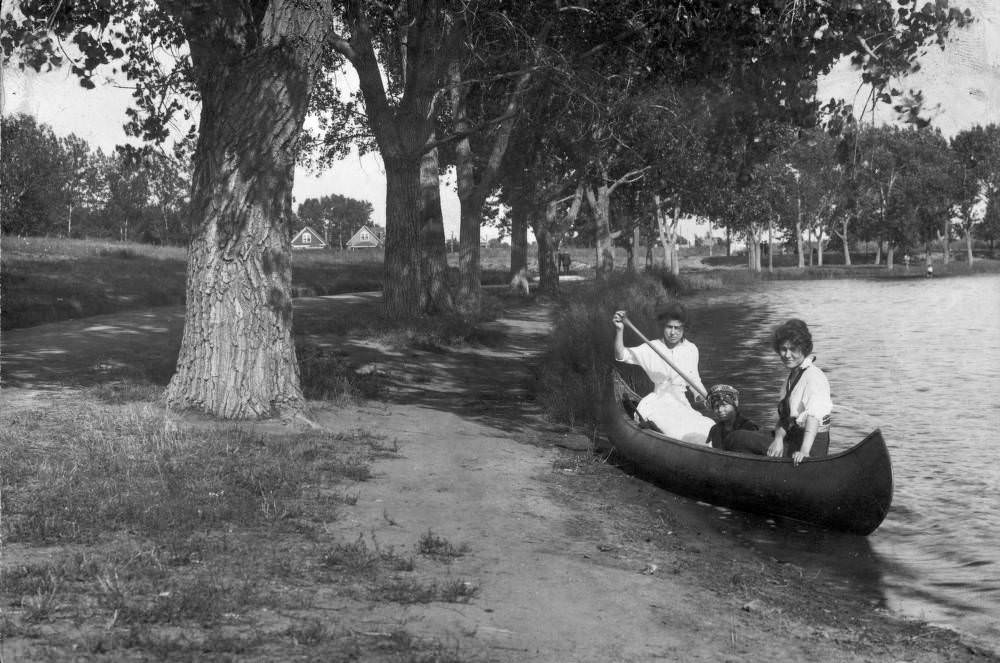 Two women and a young girl sit in a canoe near the shore of Smith Lake in Washington Park, Denver, 1909