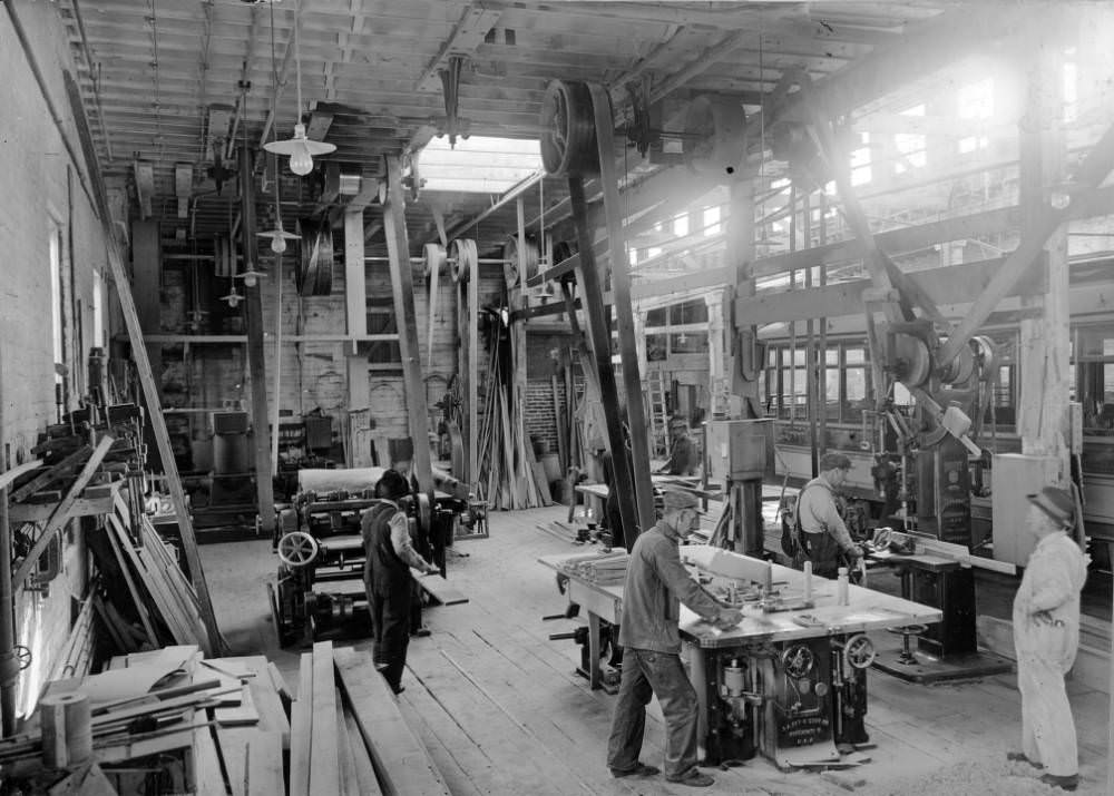 Interior of the Denver Tramway Company machine shop shows workers, benches, table saws, drills, and lumber, 1909