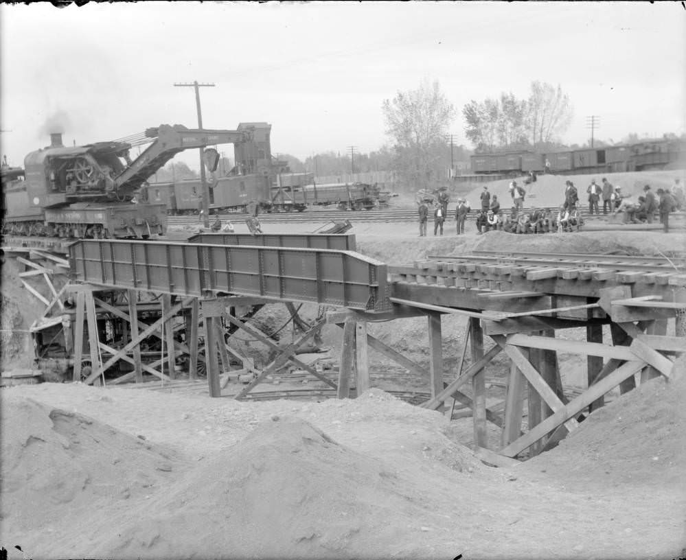 A Colorado and Southern (C&S) Railway railroad crane hoists a metal barrier for a bridge on the tracks over the Alameda Avenue underpass construction site in Denver, 1909