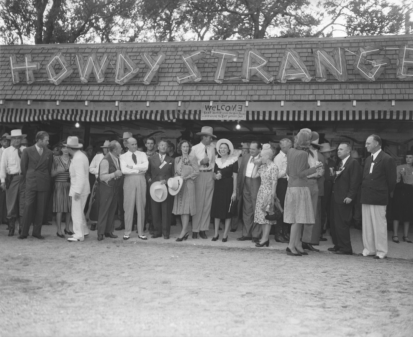 A group poses in front of a "Howdy Stranger" sign at Shady Oak Farm, 1940