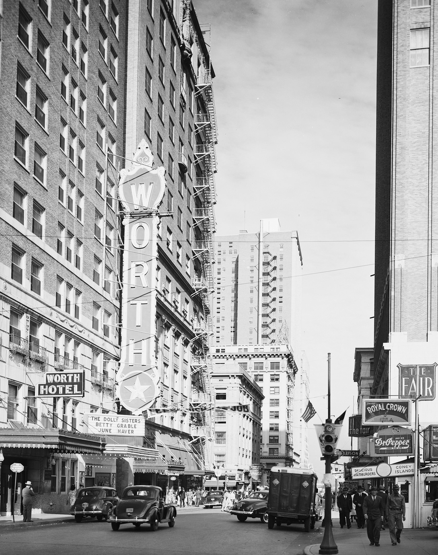 Bewley Building--Worth Hotel in foreground. People are walking on the pavement and automobiles are on the street, 1945