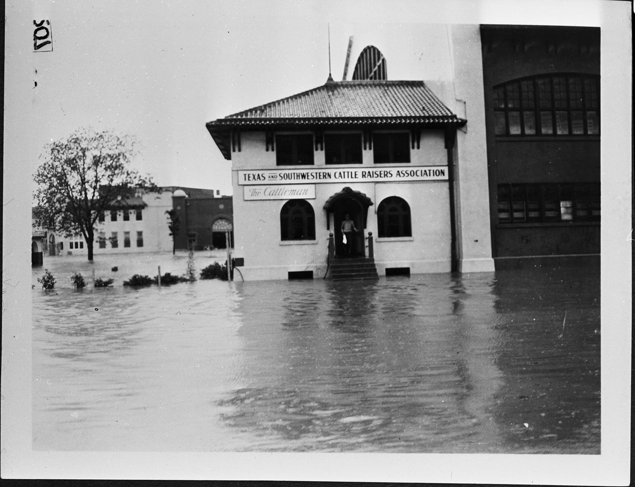 The Fort Worth Stockyards after a flood. A building has water coming up the front steps. A person is standing at the top of the steps