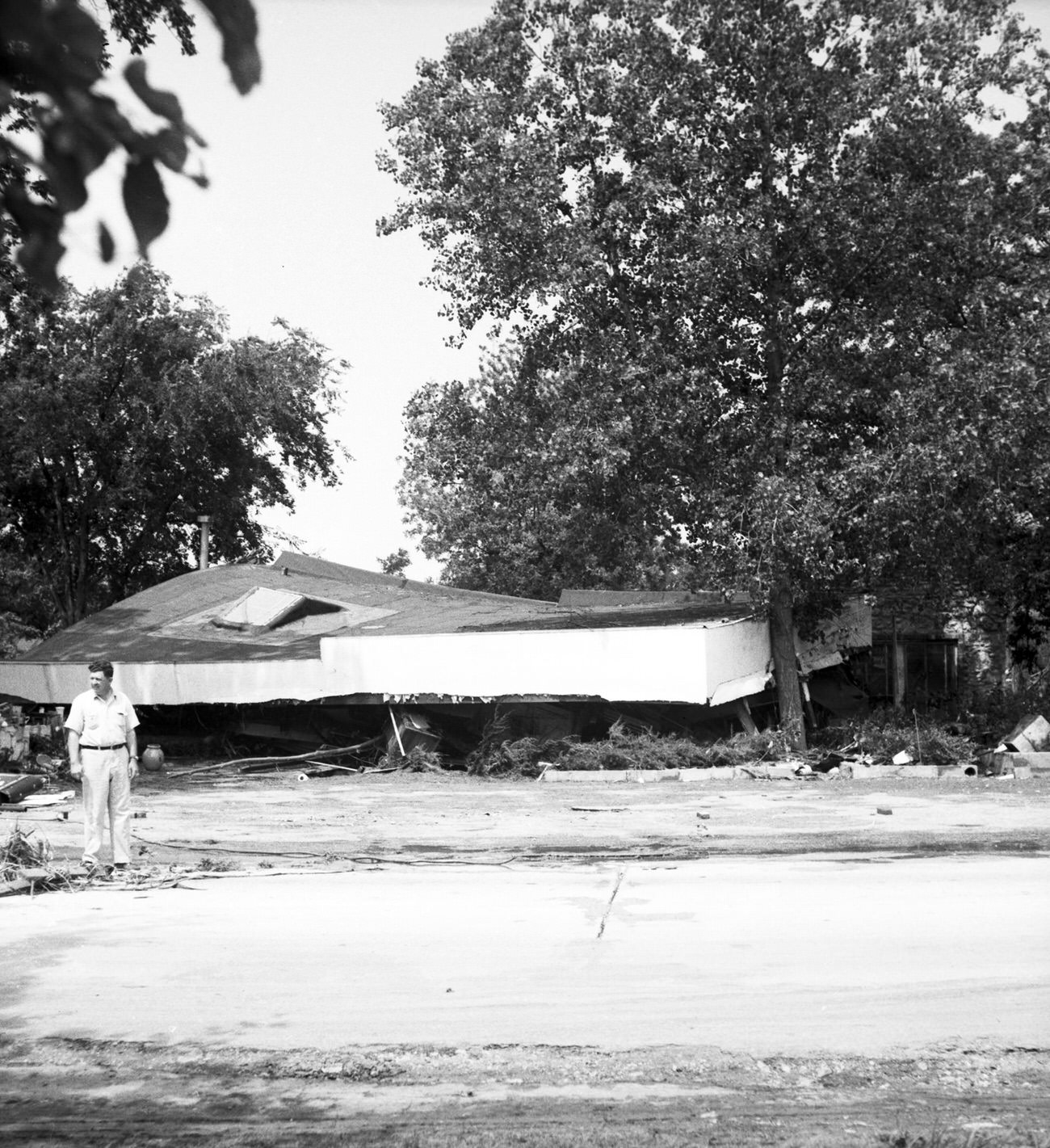 Man standing in front of remains of damaged house, 1949