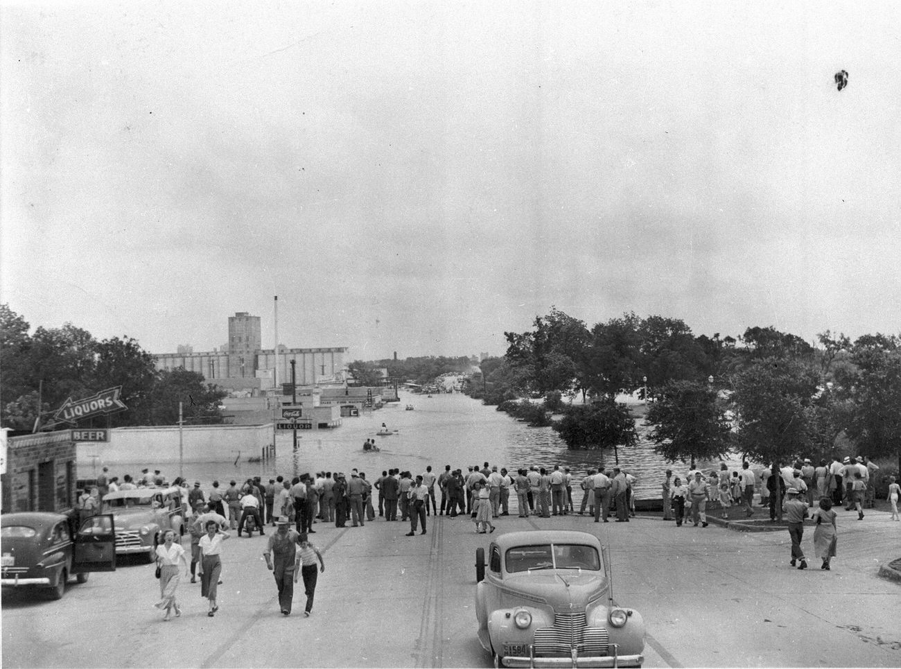 People lining street at water's edge during flood, 1949