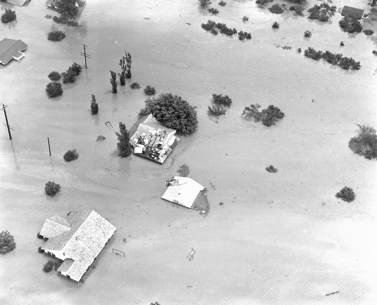 Fort Worth, Texas, flood of 1949, showing a submerged neighborhood. Atop one home sits the residents' possessions. A few people can be seen standing on the roof of another home.