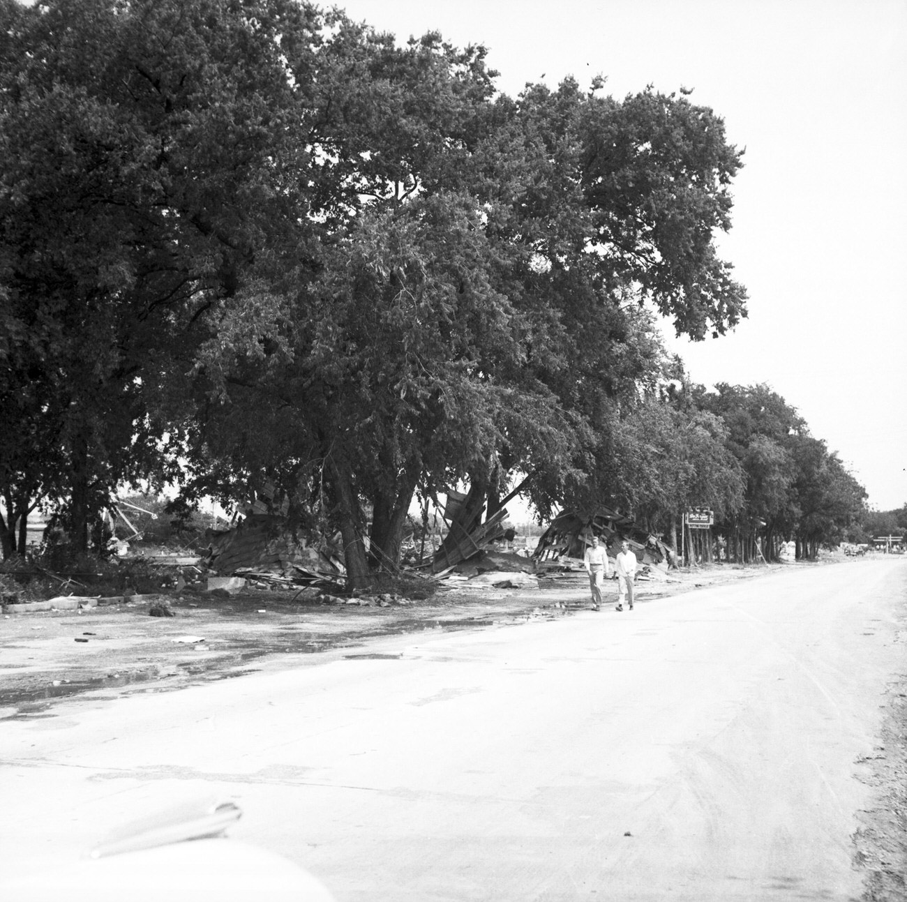 Men walking alongside debris on the side of a road after flood, 1949