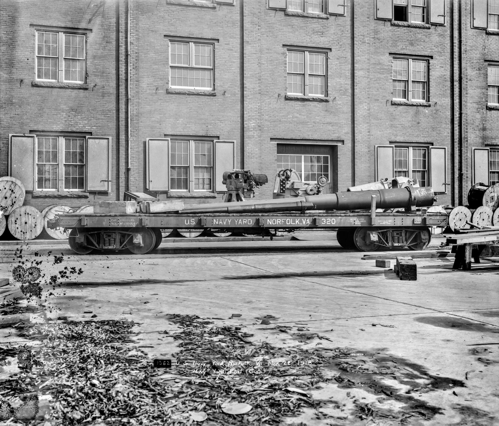 Navy Yard in Norfolk Virginia of a flat car with what looks like a large gun (barrel for a battleship) on top, 1918