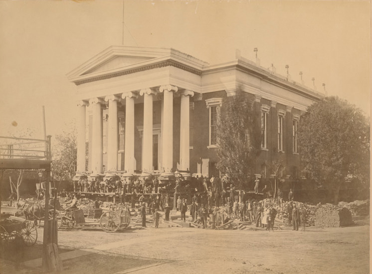 View of a Sacramento Valley R.R. train parked beside train depot on Front St. Adams McNeil wholesale grocers, 1874