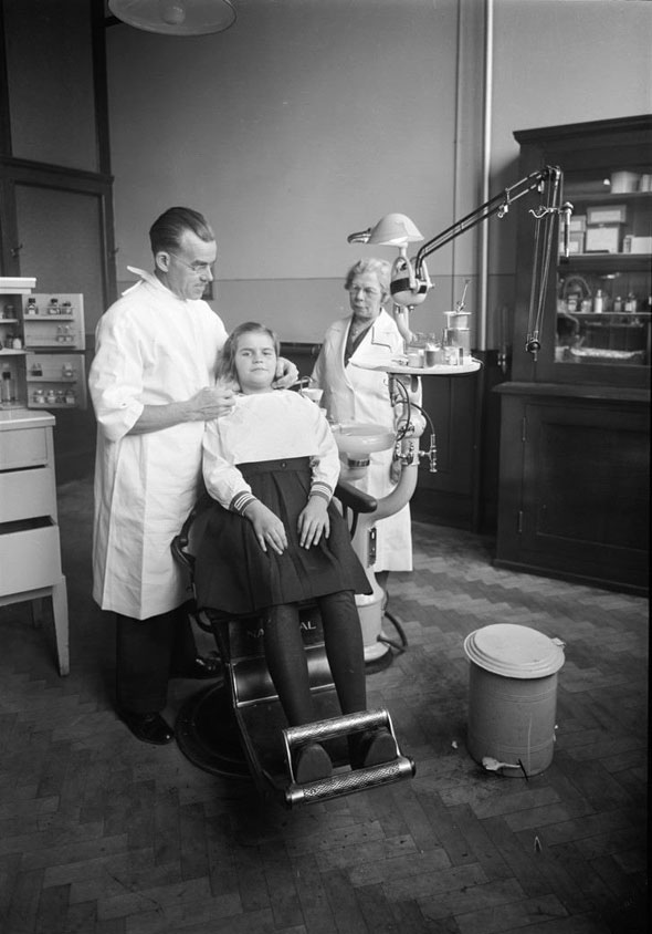 Dentist prepares to examine a girl at a high school clinic, 1940s