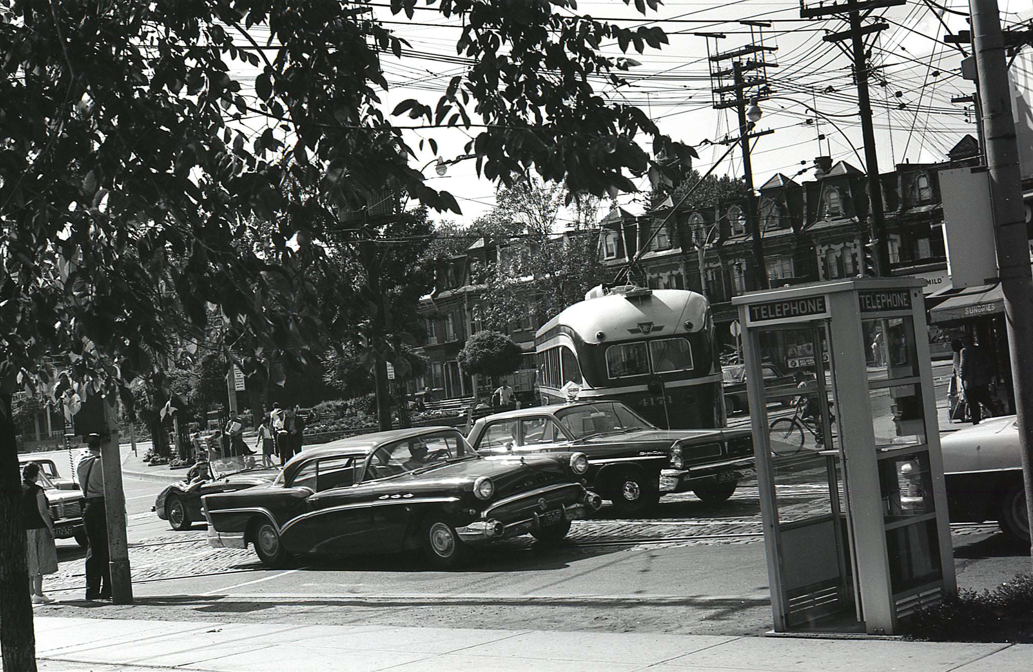 Phone booths, streetcars, and vintage vehicles at Gerrard and Parliament. Taken from the southeast corner, looking northwest across the island parkette in 1963