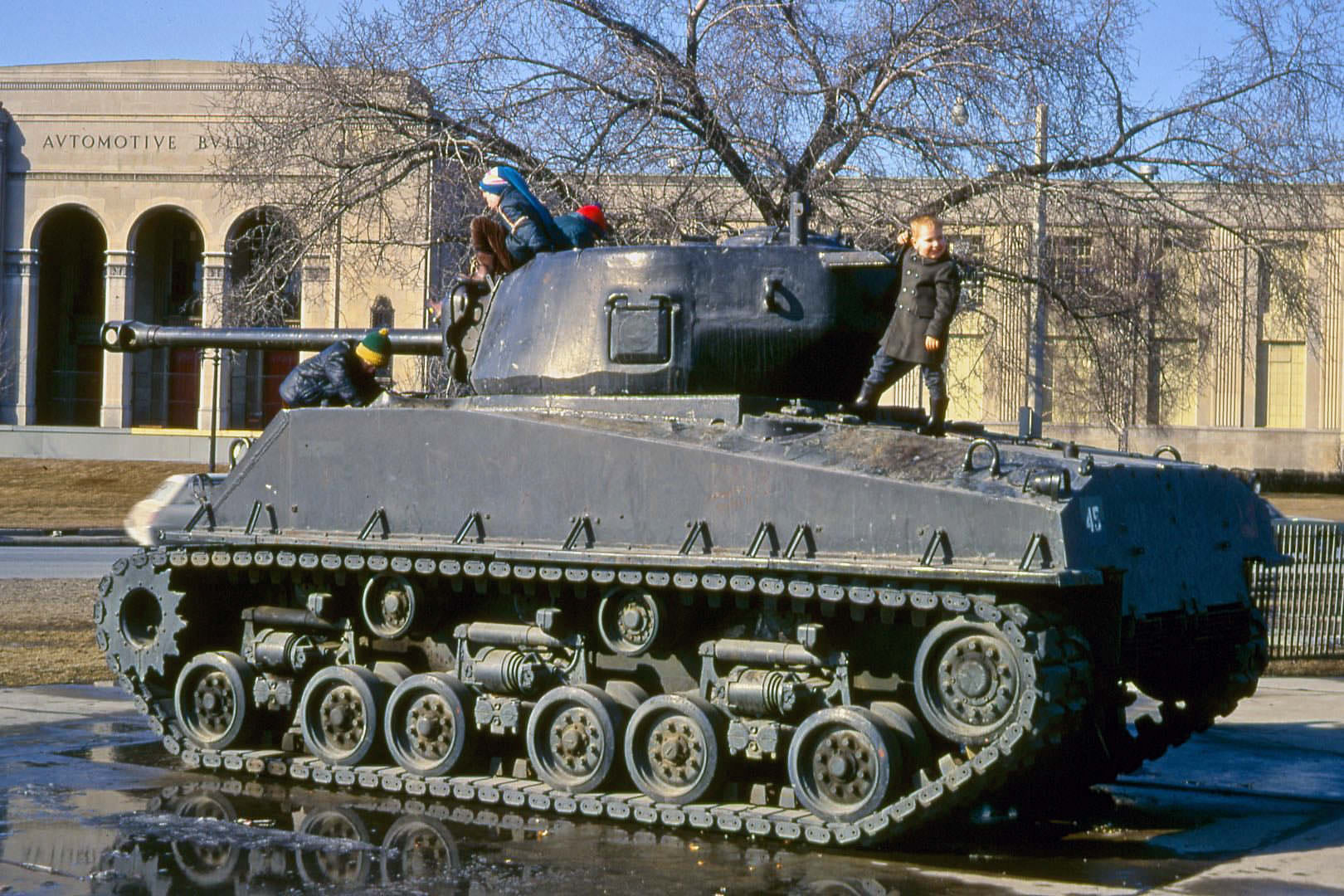 Kids play on a retired Sherman tank, across the street from the Automotive Building, 1970