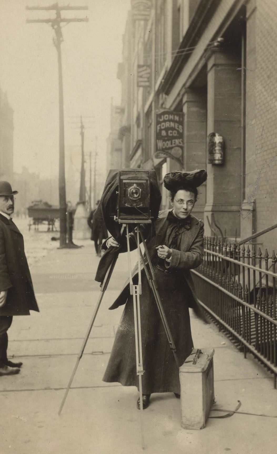 Portrait of Jessie Tarbox Beals standing on a city sidewalk with her camera, 1920