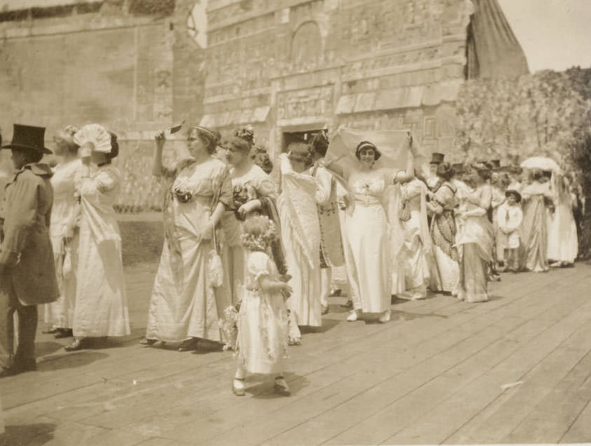 A young flower girl girl turns to look at the women in 19th century costume for the Marquis de Lafayette's ball in 1825 St. Louis, a scene in the Pageant, Pageant and Masque of St. Louis.