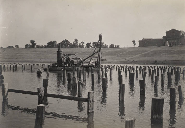 Men using machinery to drive piers into the water of the Grand Basin, Forest Park, for construction of the stage for the Pageant and Masque of St. Louis, 1914