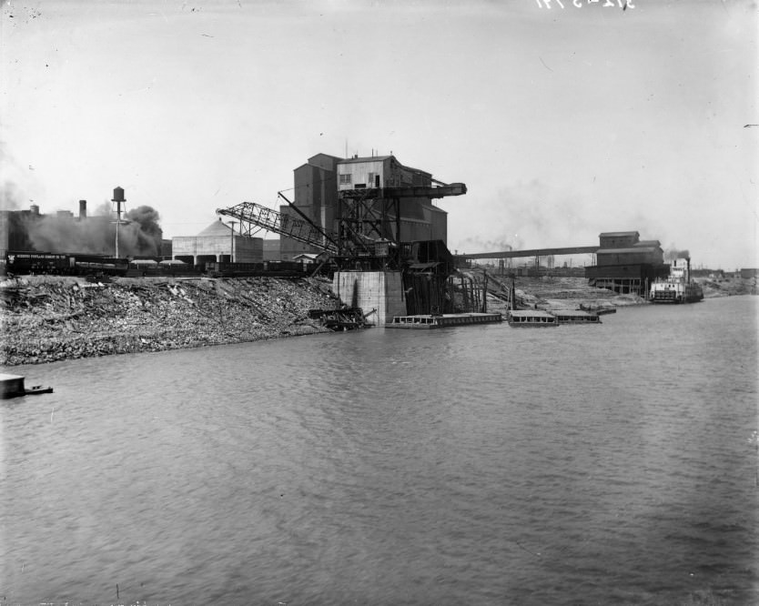 The Missouri Portland Cement Company factory and loading docks on the Mississippi River. A steamboat (the Belle of Calhoun) is visible in the background at one of the docks, 1910