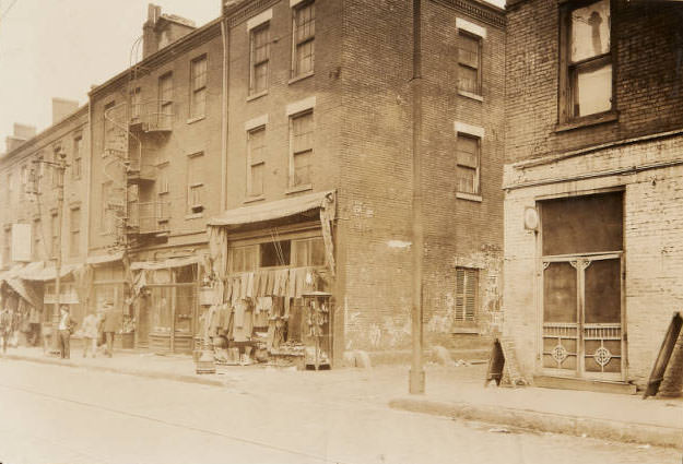 A row of storefronts located near the intersection of Sixth Street and Franklin Avenue. A clothing store displays its wares on the sidewalk, 1910