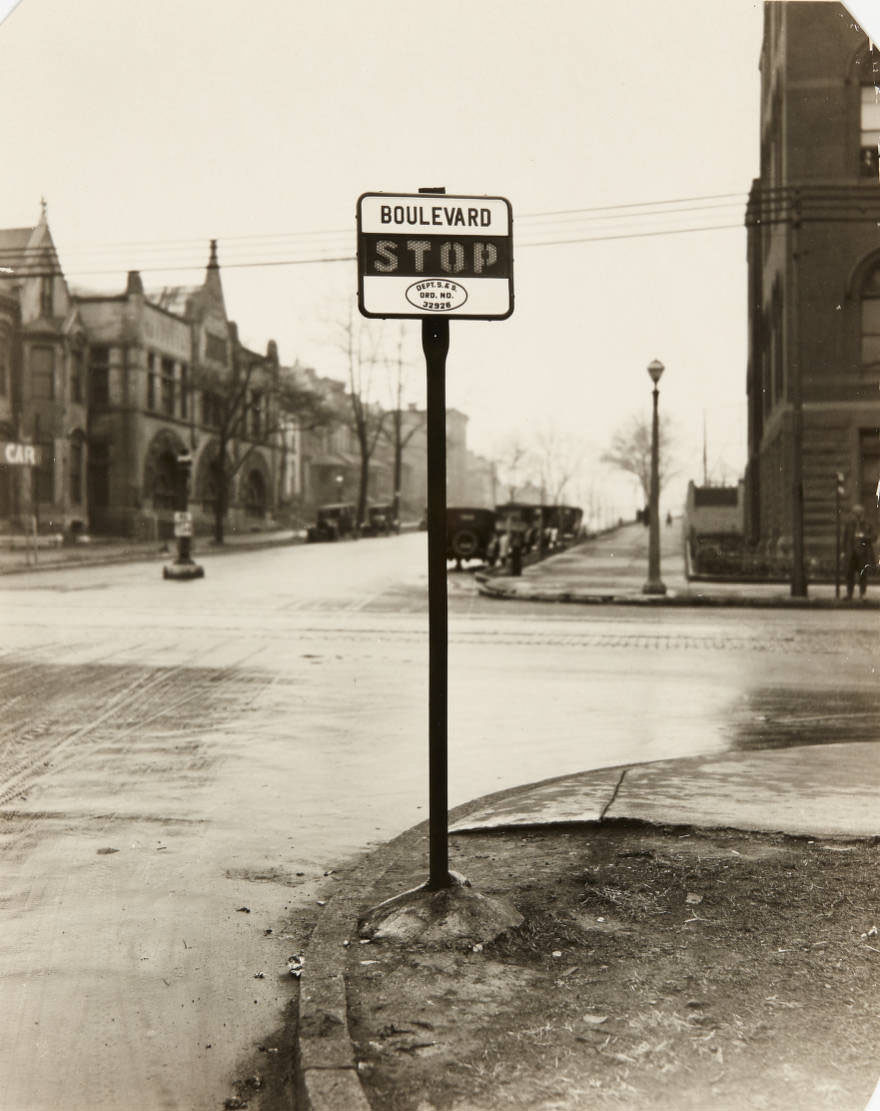 A stop sign on the corner of West Pine Blvd. at its intersection with Grand, looking west, 1915