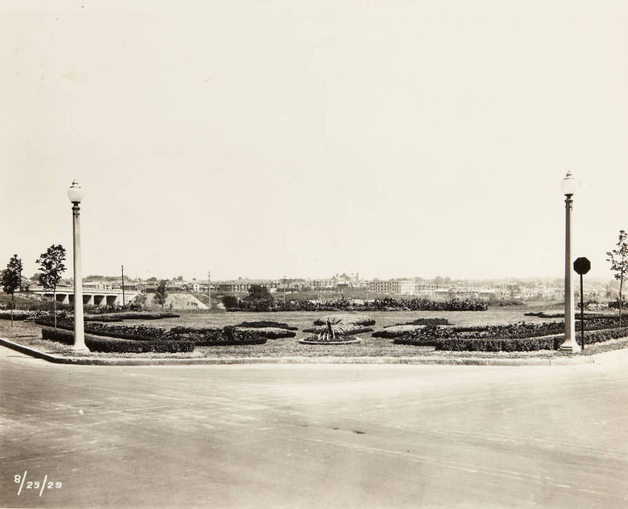 A well-maintained greenspace with trimmed hedges and flower beds at an unidentified intersection, 1910s