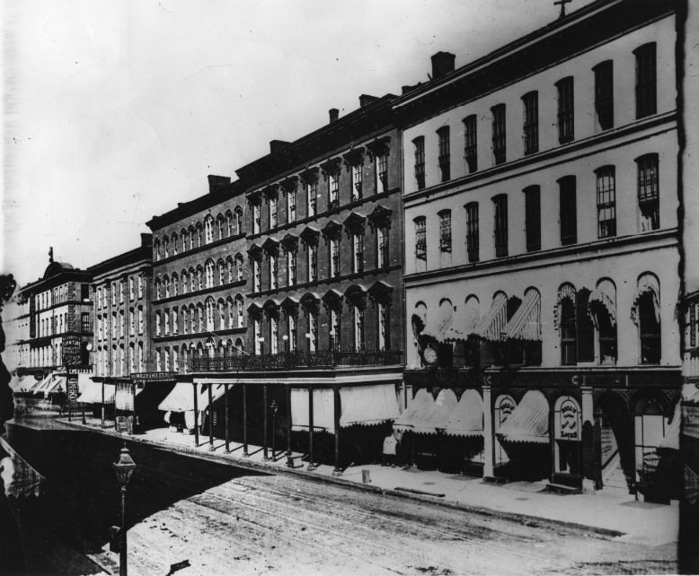 The east side of Fourth street between Olive and Locust, showing the Everett House, Pingee & Brown, Prop., with the upper veranda and iron railing which formed a hotel's trademark, 1875
