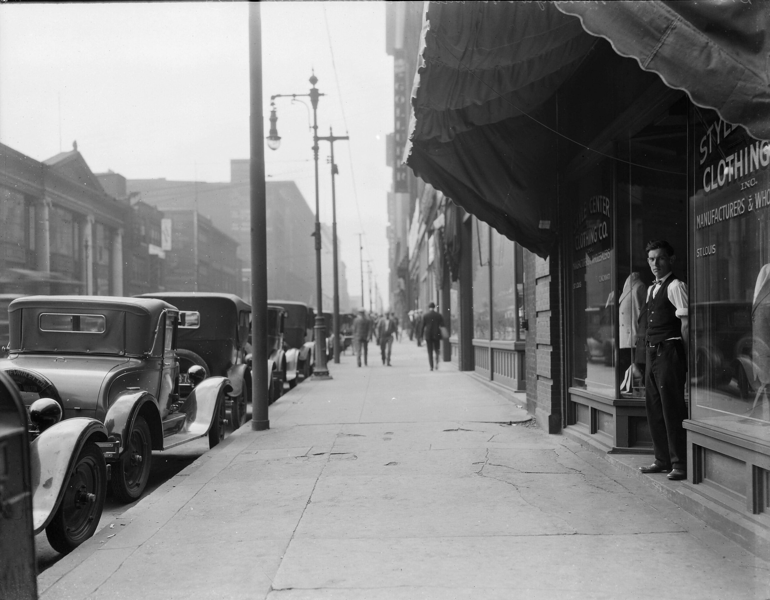 View of a young man standing in the doorway at Style Center Clothing Co. on the north side of the 1300 block of Washington Avenue looking west, 1925