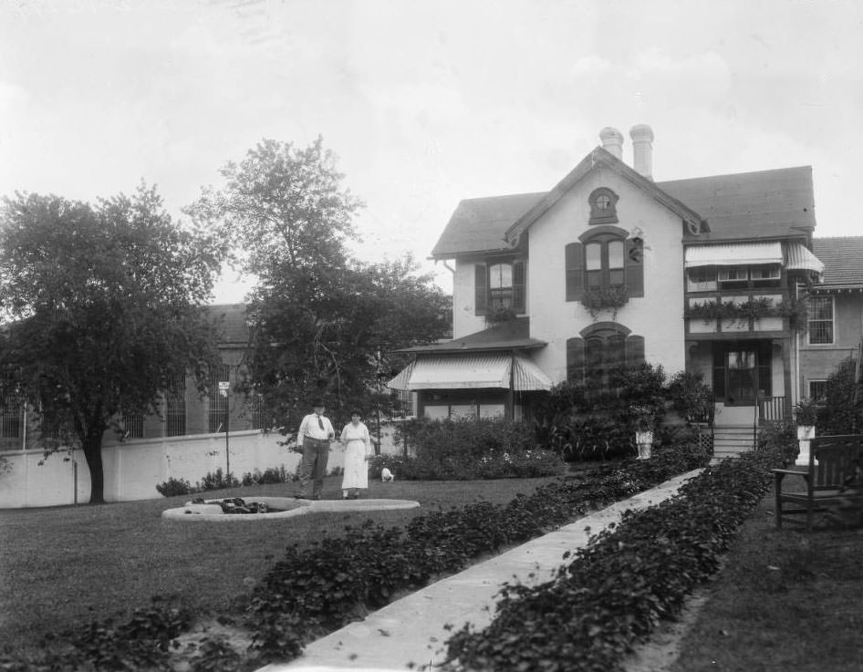 View of a man, woman (and dog) posing on the grounds at the Superintendent’s residence of the St. Louis City Workhouse at the SE corner of South Broadway & Meramec Street.