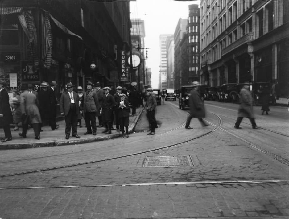 View of looking east on Locust at 7th of several men and boys standing on the corner in front of Judge & Dolph's Drugstore, 1925