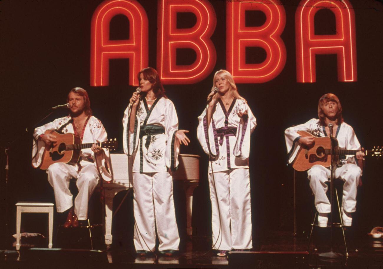 Benny Andersson, Frida Lyngstad, Agnetha Faltskog, Bjorn Ulvaeus), wearing similar white Asian-influenced costumes, perform for the television program Midnight Special with a neon