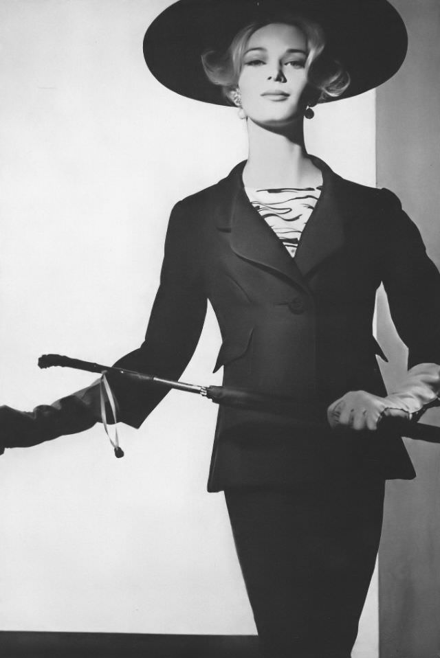 Anne de Zogheb in black silk worsted suit with a long flaring jacket worn with a black and white zebra-striped silk blouse, by Adele Simpson, hat by Mr. Arnold, January 1, 1962