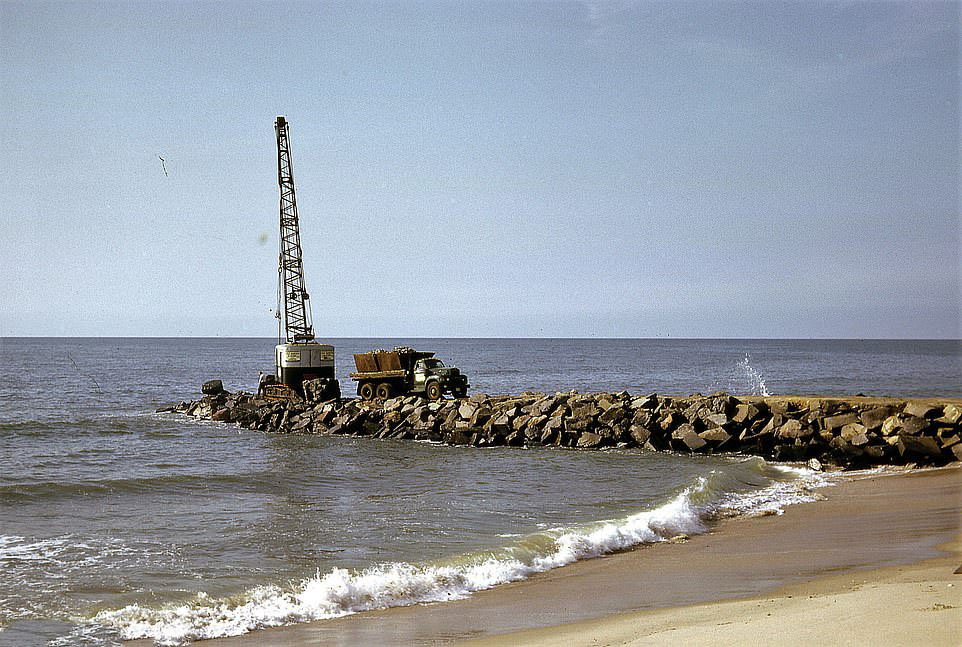 A truck drives away from a small crane that had been placed at the end of a shore defence