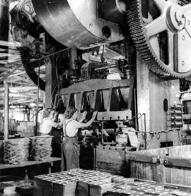 Two young woman working at a large press used for making parts of ammunition boxes.